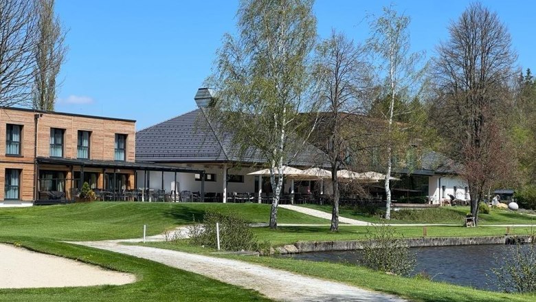 Modernes Gebäude mit Terrasse am See, umgeben von Bäumen und Rasen., © Hotel-Restaurant Hausschachen