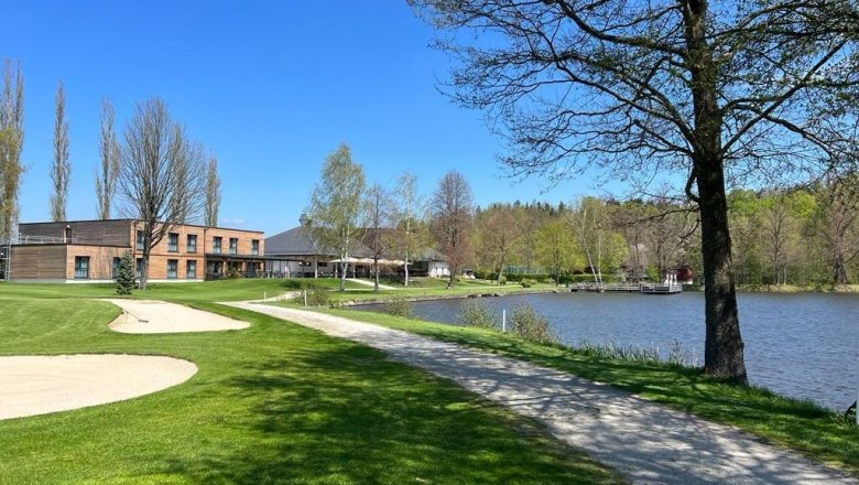 Golfplatz mit Clubhaus am See, umgeben von Bäumen und blauem Himmel., © Hotel-Restaurant Hausschachen